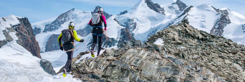 Due alpinisti corrono su una cresta in una cornice di montagne innevate